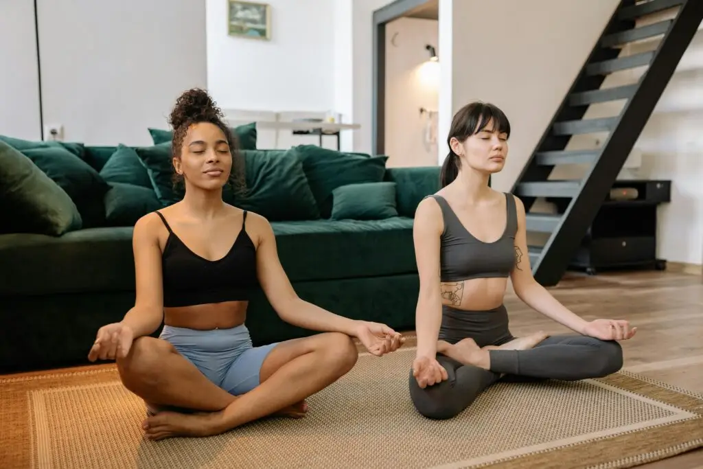 Two women practicing meditation and yoga indoors, promoting relaxation and mental wellness.