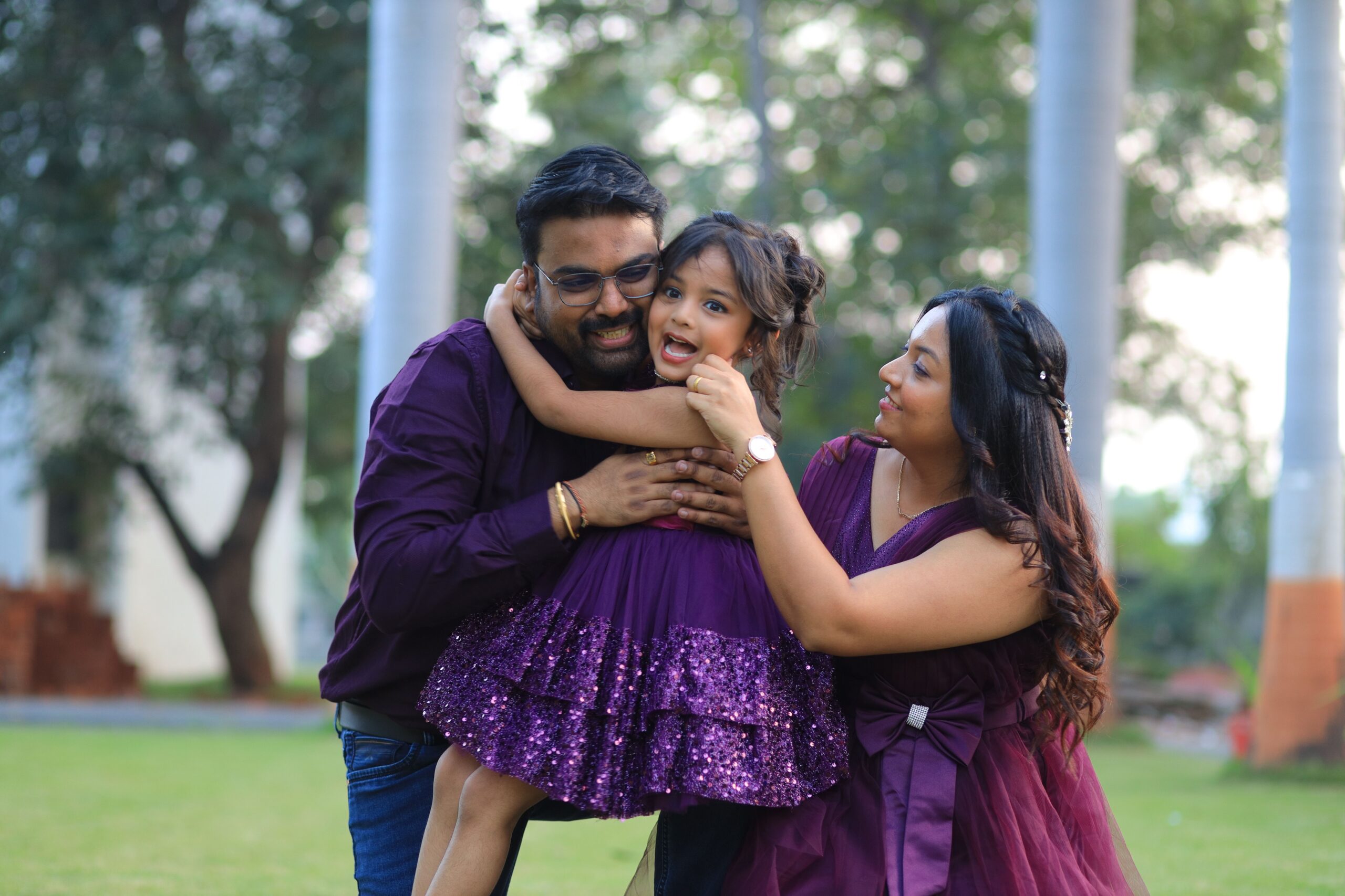 A happy family embraces outdoors, wearing matching purple outfits, capturing a moment of love and joy.